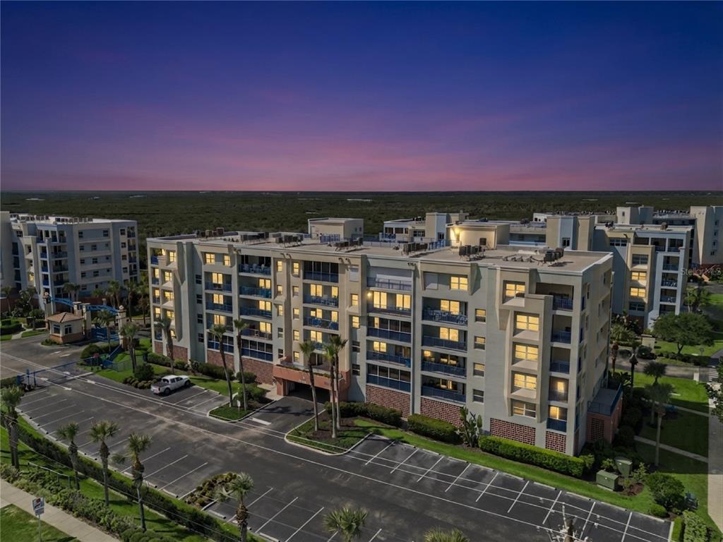 An aerial view of a multi-story apartment building with a parking lot at dusk — 5300 S ATLANTIC AVENUE UNIT 13-604, NEW SMYRNA BEACH, FL
