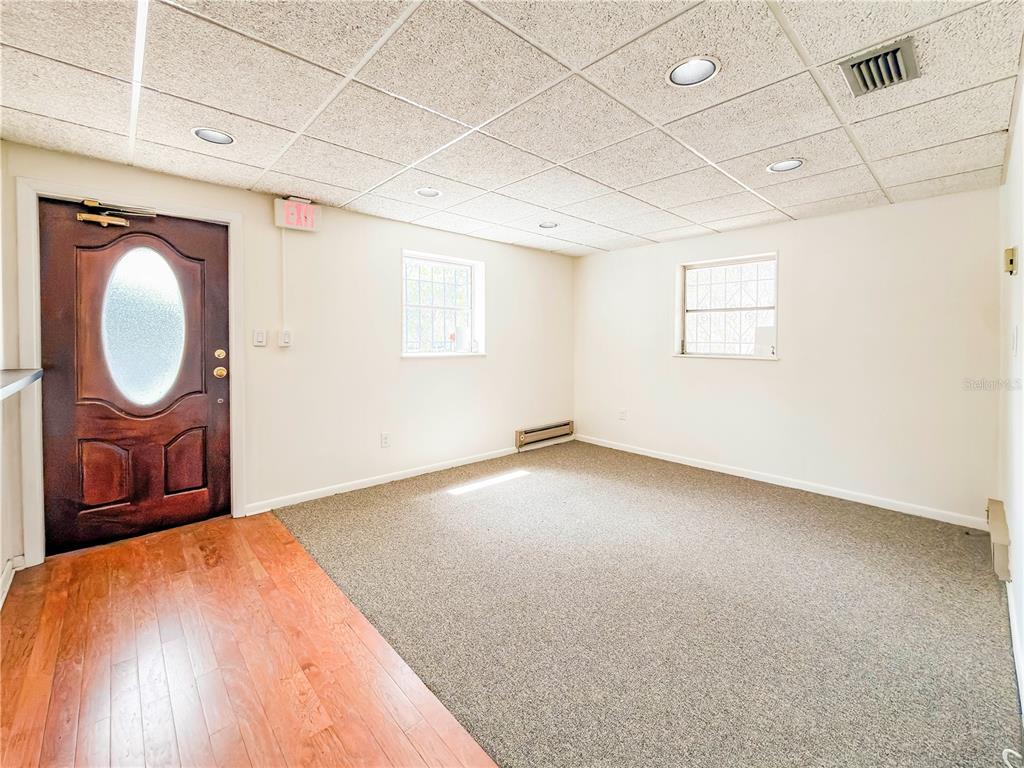 A room with a drop ceiling, carpeted floor, wood entryway, and two windows with security bars — 703 E PINE STREET, ORLANDO, FL