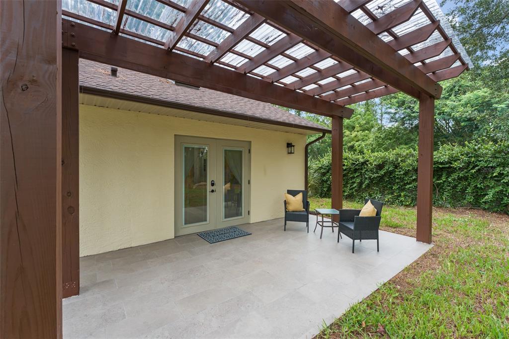A patio with a wooden pergola, tiled flooring, and two chairs sits outside a house — 5028 AUTUMN RIDGE LANE, WINDERMERE, FL