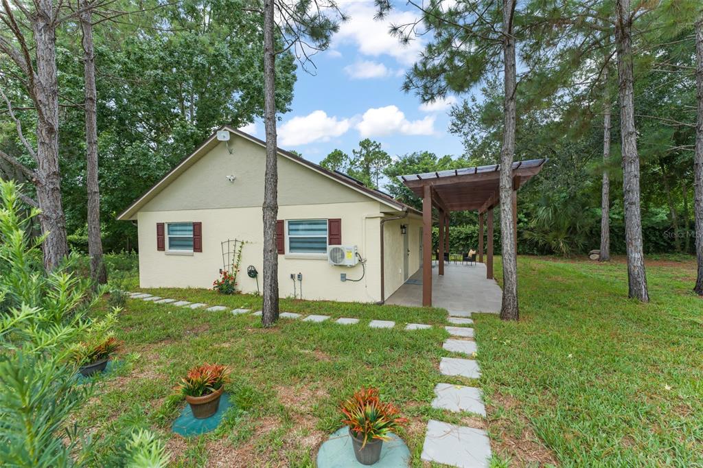 A single-story house exterior features a covered patio, a stone walkway, and surrounding pine trees — 5028 AUTUMN RIDGE LANE, WINDERMERE, FL