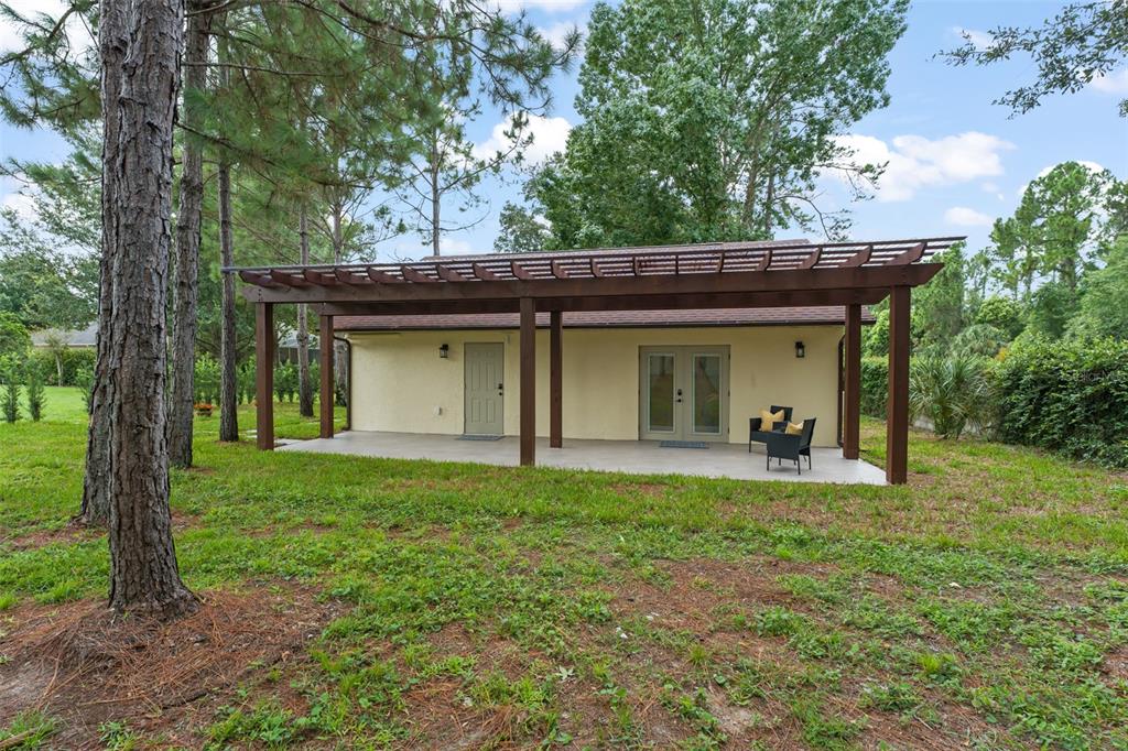 A detached building with a covered patio, pergola, and French doors sits in a wooded yard — 5028 AUTUMN RIDGE LANE, WINDERMERE, FL