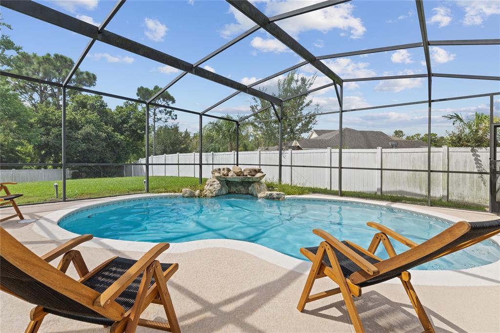 A screened-in swimming pool with a rock waterfall feature sits in a backyard with chairs — 14424 BABYLON WAY, ORLANDO, FL