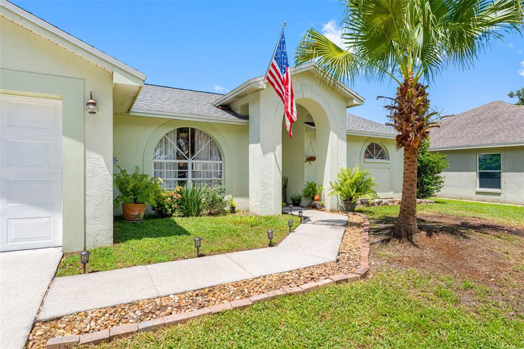 A light-colored house features an arched entryway, a palm tree, and an American flag — 1742 STAYSAIL DRIVE, VALRICO, FL