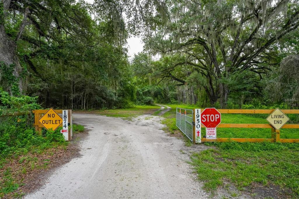 A dirt driveway forks between two wooden fences with address signs and a stop sign — SE 14TH TERRACE, BUSHNELL, FL