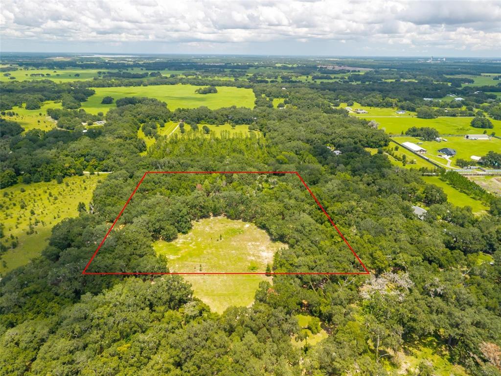An aerial view shows a rectangular plot of land outlined in red amidst wooded acreage — SE 14TH TERRACE, BUSHNELL, FL