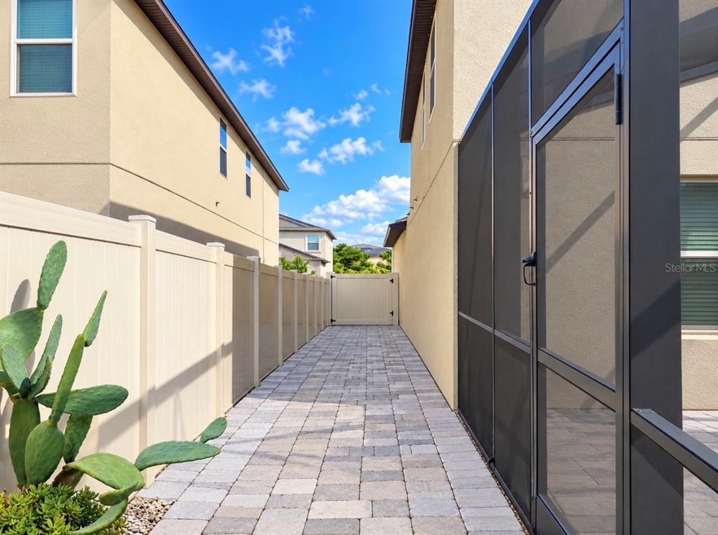 A paved side yard walkway sits between a house wall and a tall vinyl fence — 15705 FORT ISLAND PLACE, SUN CITY CENTER, FL