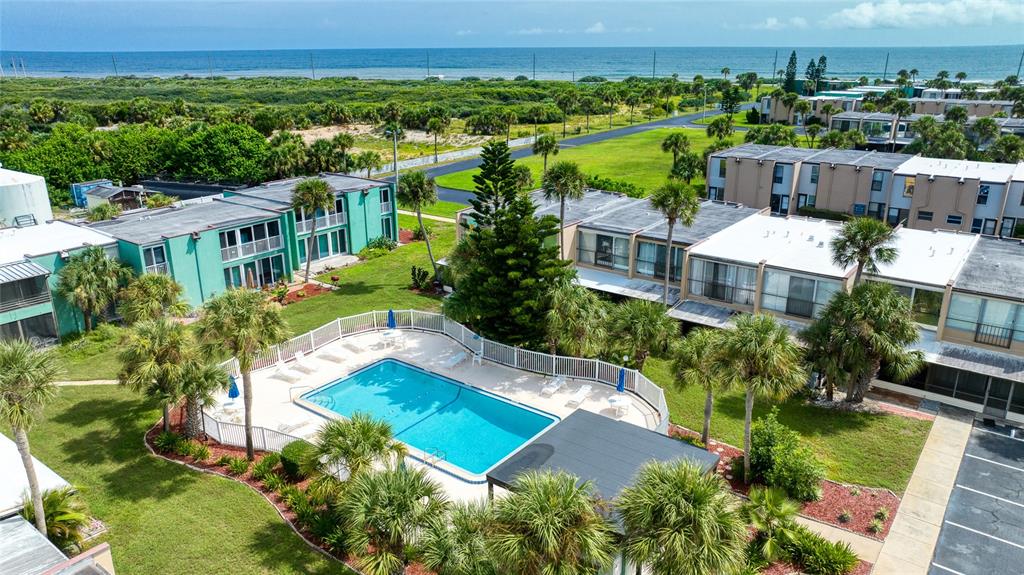 An aerial view shows a swimming pool surrounded by palm trees and multi-story apartment buildings — 5500 OCEAN SHORE BOULEVARD UNIT UT58, ORMOND BEACH, FL