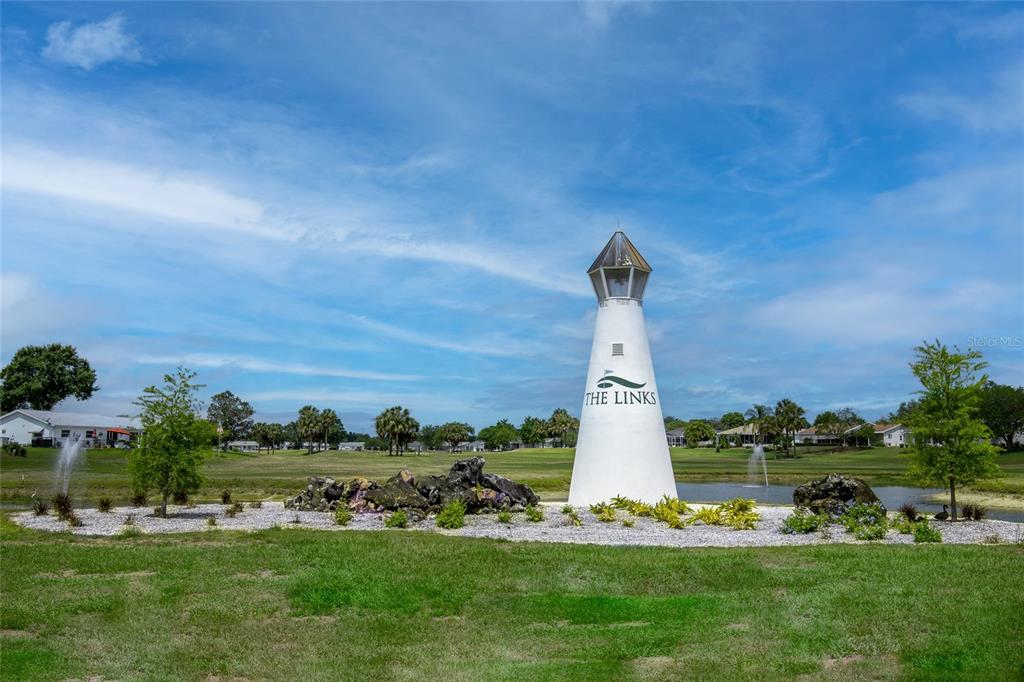A white lighthouse structure stands on a grassy lawn near a pond and golf course — 10731 SE 174TH LOOP, SUMMERFIELD, FL