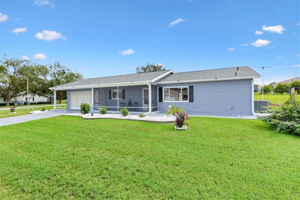 A blue single-story house with a white-trimmed porch and a green lawn under a blue sky — 10731 SE 174TH LOOP, SUMMERFIELD, FL
