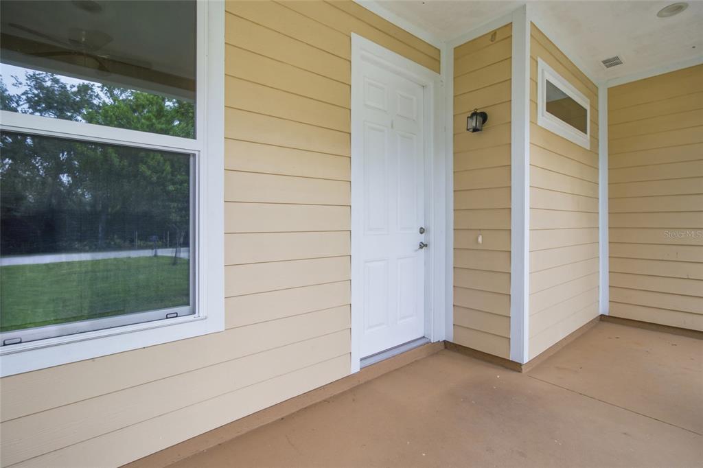 A covered porch with yellow lap siding, a white door, and a large window — 4510 WILKINSON ROAD, SARASOTA, FL