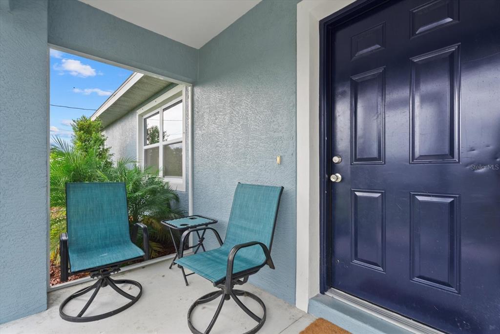 A covered porch features two teal patio chairs, a small table, and a dark blue door — 8288 SW SUNNYBREEZE ROAD, ARCADIA, FL