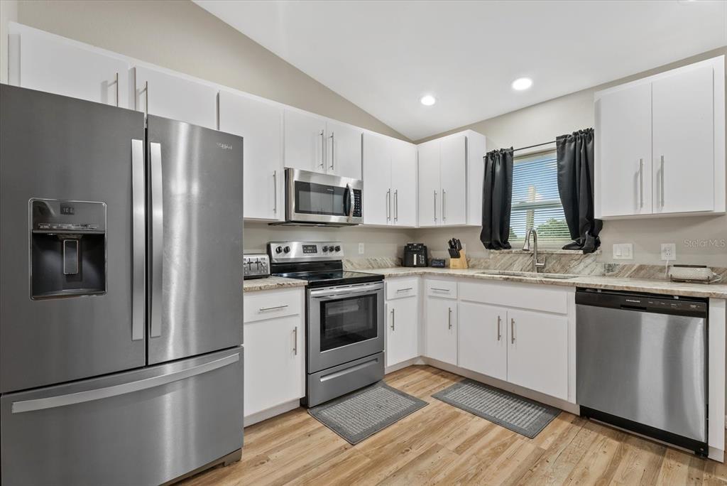 A kitchen features white cabinets, stainless steel appliances, granite countertops, and wood-look flooring — 8288 SW SUNNYBREEZE ROAD, ARCADIA, FL
