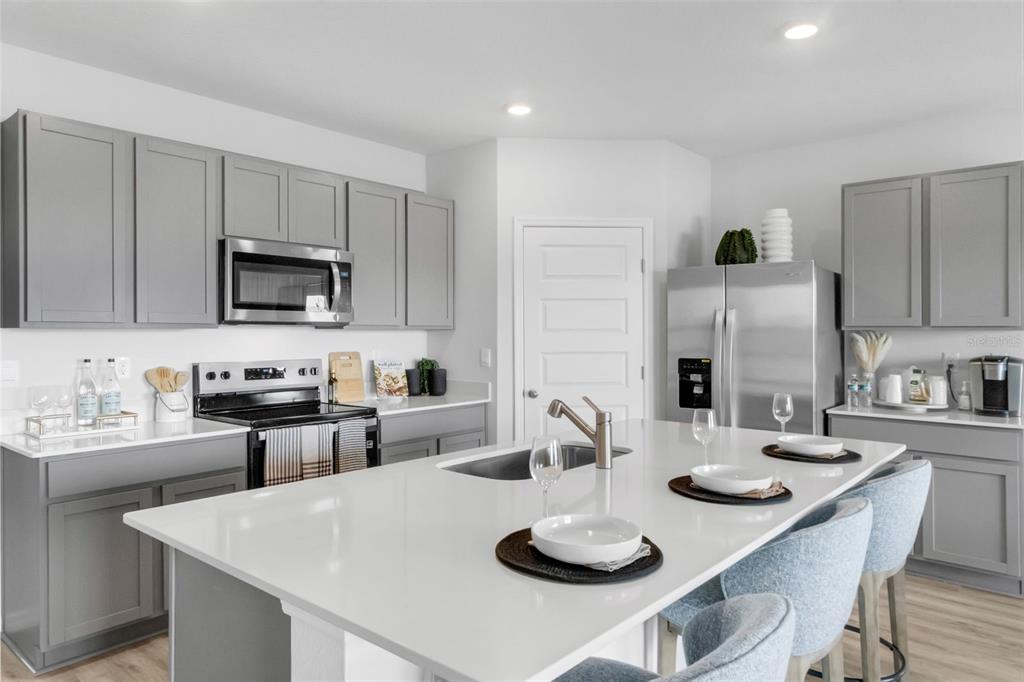 A modern kitchen features gray cabinets, white countertops, a central island, and stainless steel appliances — 7864 FORREST FOX WAY, LAKELAND, FL