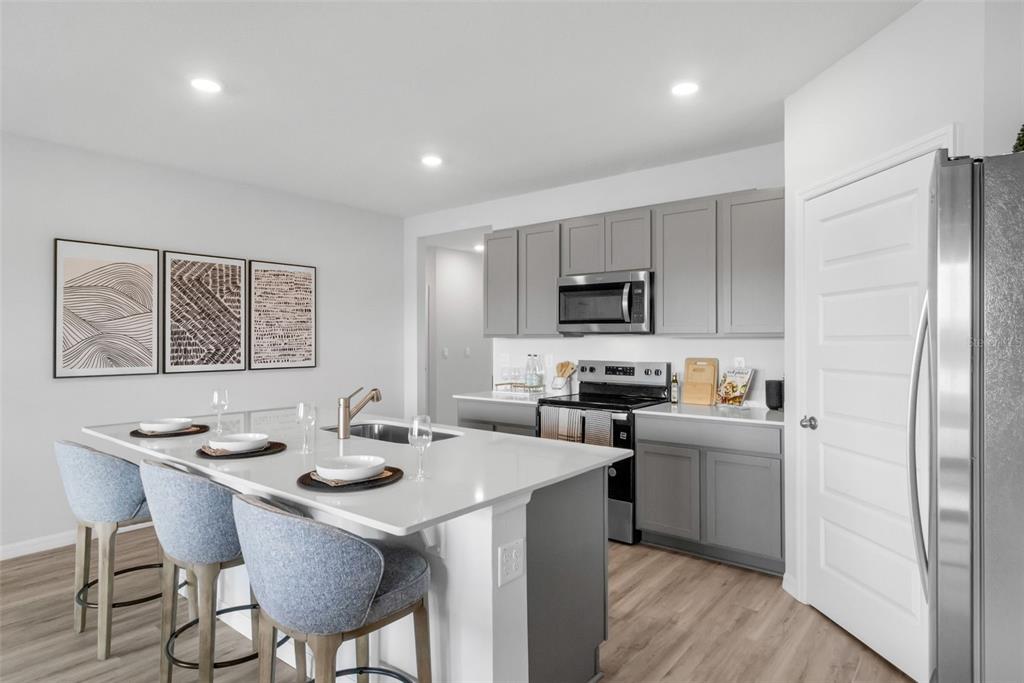 A modern kitchen features a white quartz island, gray cabinetry, and light wood-look flooring — 7864 FORREST FOX WAY, LAKELAND, FL