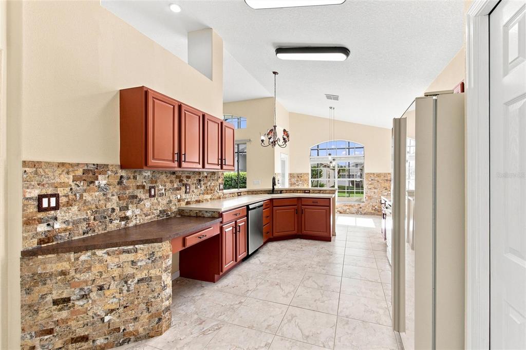 A kitchen features reddish-brown cabinets, a stone tile backsplash, and light-colored floor tiles — 140 MOSS LN, DAVENPORT, FL