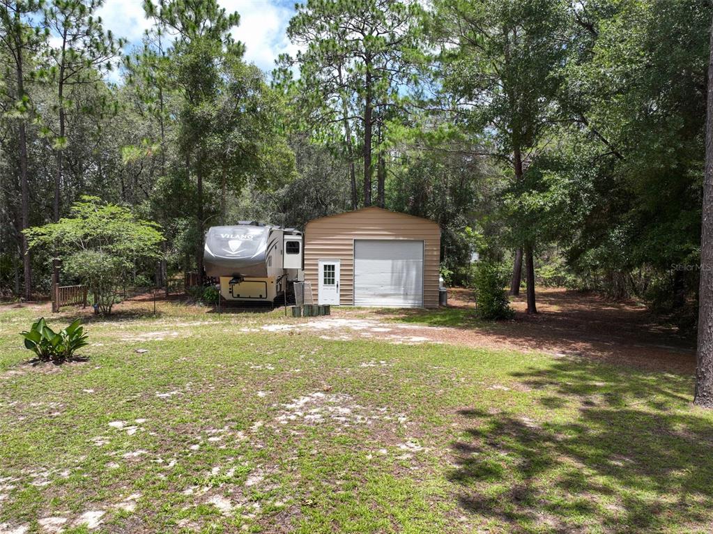 A metal shed and a fifth-wheel RV sit in a wooded, grassy yard — 5620 LASSEN STREET, KEYSTONE HEIGHTS, FL