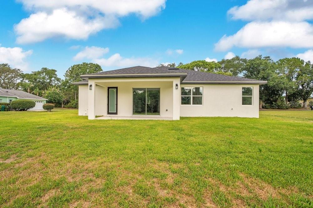 The rear exterior of a single-story house features a covered patio and a grassy yard — 551 DOWLING CIRCLE, LADY LAKE, FL
