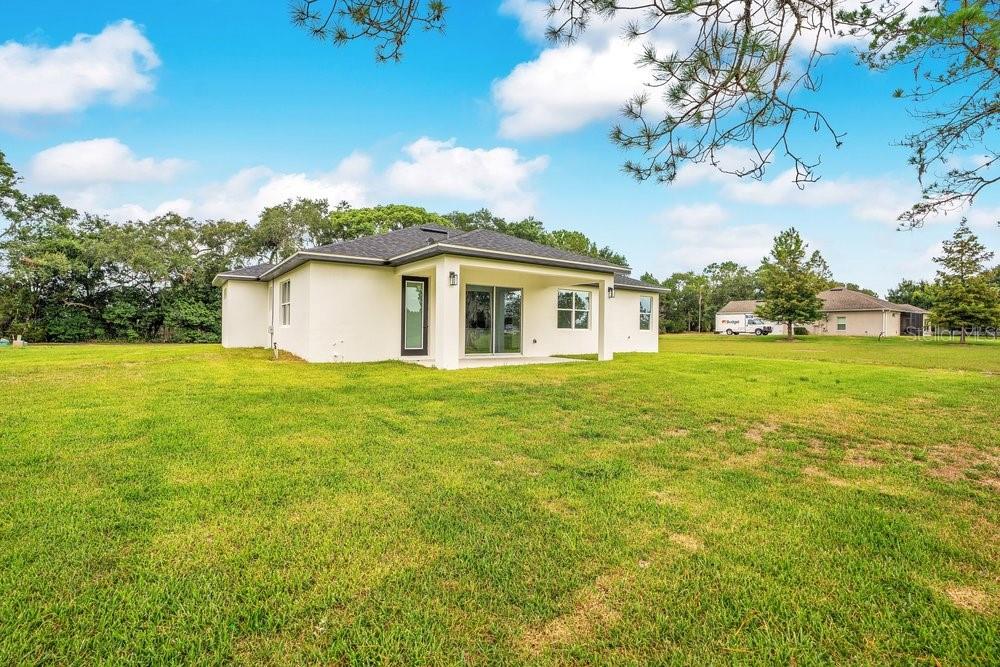 The exterior rear view of a single-story white house with a covered patio and lawn — 551 DOWLING CIRCLE, LADY LAKE, FL