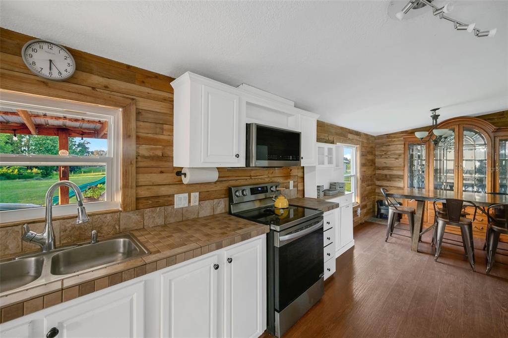 A kitchen features white cabinets, a tiled countertop, stainless steel appliances, and wood-paneled walls — 3858 E KNIGHTS GRIFFIN ROAD, PLANT CITY, FL