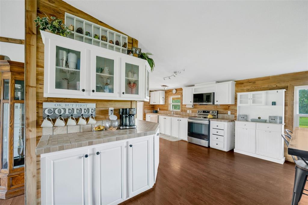 A kitchen features white cabinetry, wood-paneled walls, tile countertops, and dark wood flooring — 3858 E KNIGHTS GRIFFIN ROAD, PLANT CITY, FL