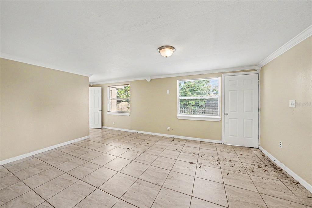 An empty room with beige walls, tile flooring, two windows, and two white doors — 10118 114TH TERRACE, LARGO, FL