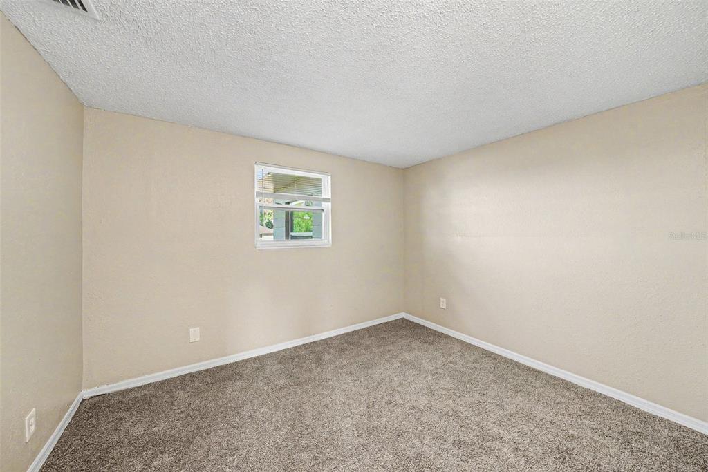 An empty bedroom with beige walls, gray carpet, and a single window — 10118 114TH TERRACE, LARGO, FL
