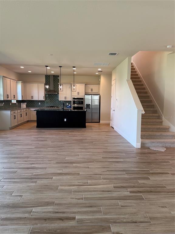 A kitchen with white cabinets, a black island, and wood-look tile flooring near a staircase — 5279 BUTTONSAGE DRIVE, ST CLOUD, FL