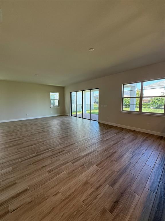 An empty living area features wood-look tile flooring, large windows, and sliding glass patio doors — 5279 BUTTONSAGE DRIVE, ST CLOUD, FL