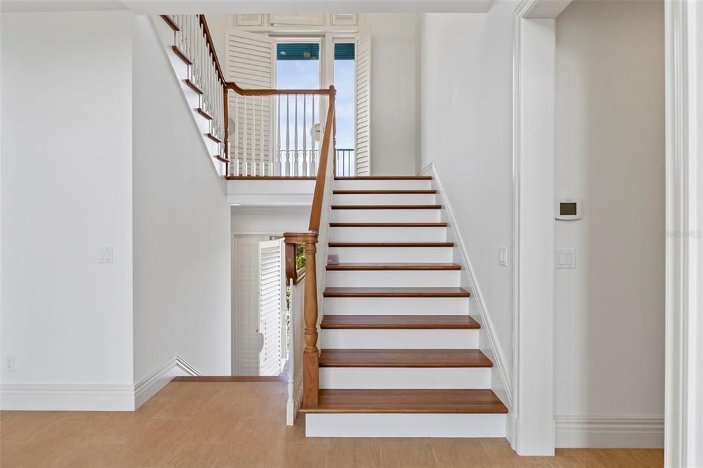 A staircase with wooden treads and white risers leads to a landing with a balcony — 2275 GENESEA LANE, VERO BEACH, FL