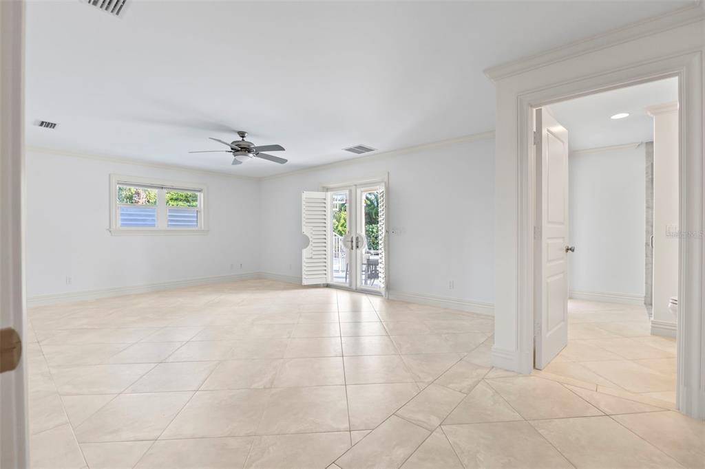 A spacious, white-walled room features light-colored tile flooring, a ceiling fan, and French doors — 2275 GENESEA LANE, VERO BEACH, FL