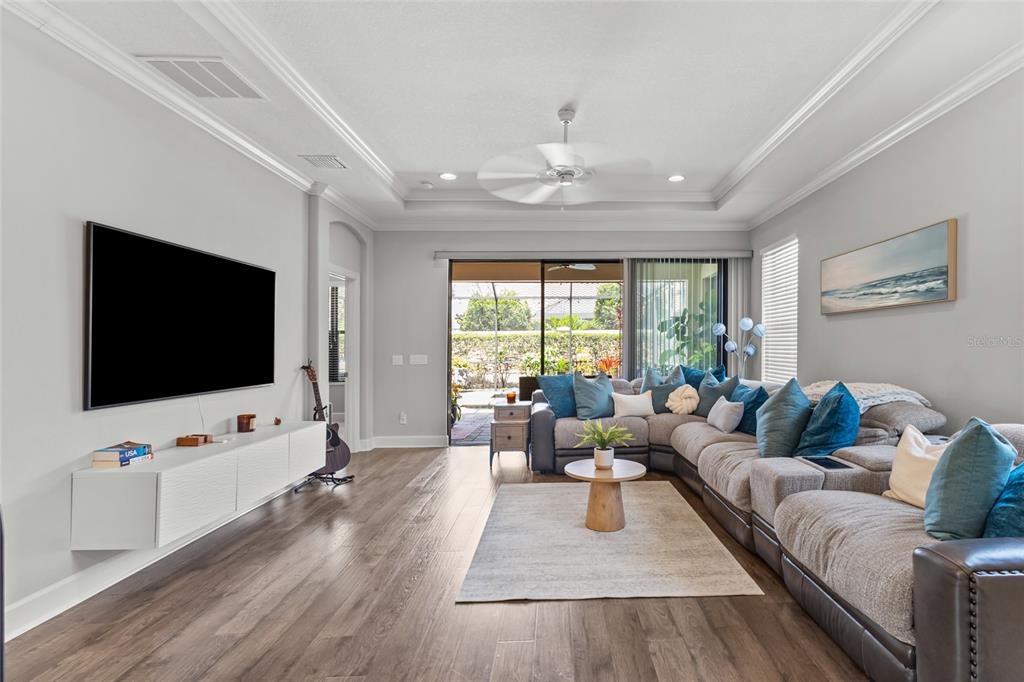 A living room features a desk, a wall-mounted television, and a sectional sofa on wood floors — 5019 SAVONA RUN, BRADENTON, FL