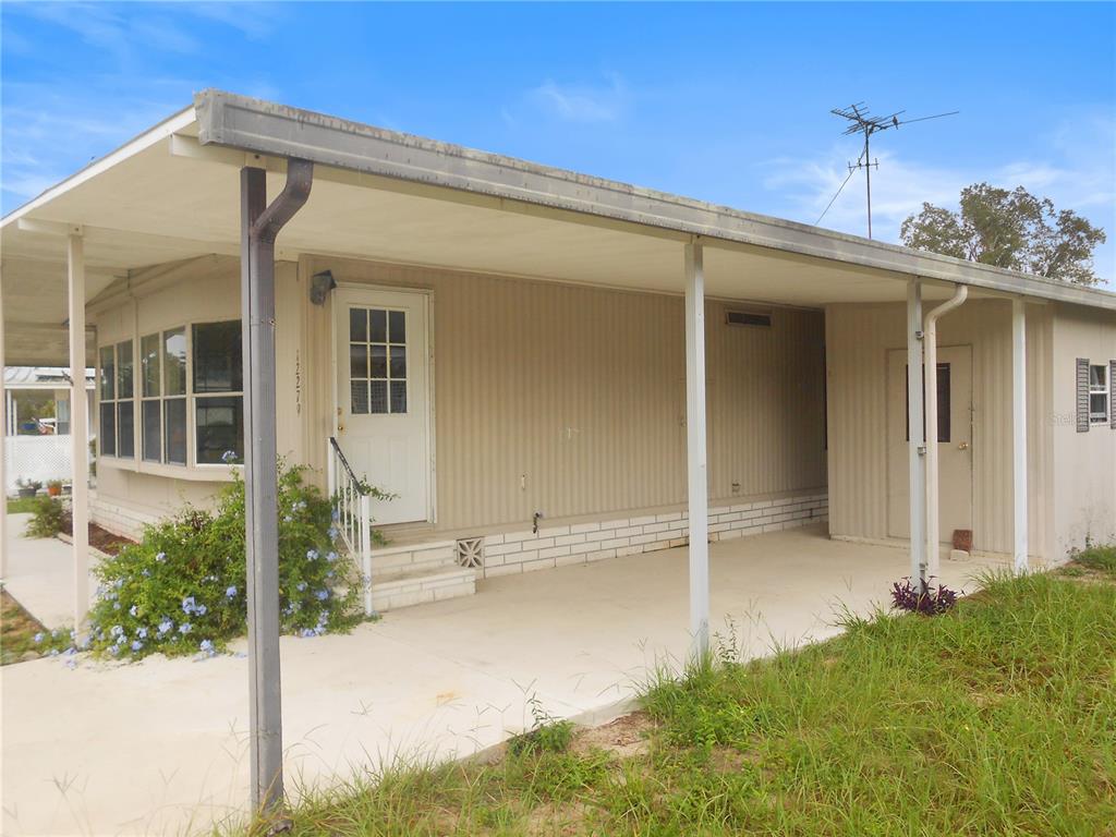 A single-story mobile home features a covered carport, a white front door, and light-colored siding — 12279 OBRIEN AVENUE, BROOKSVILLE, FL