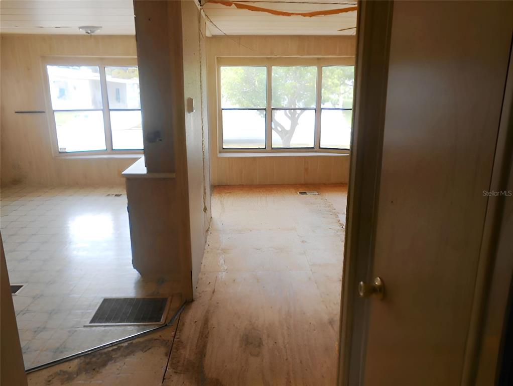 An interior view shows a room with exposed subflooring, wood-paneled walls, and large windows — 12279 OBRIEN AVENUE, BROOKSVILLE, FL
