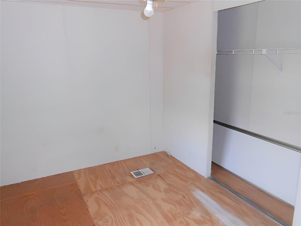 An unfinished room with plywood flooring, white walls, and an open closet with shelving — 12279 OBRIEN AVENUE, BROOKSVILLE, FL