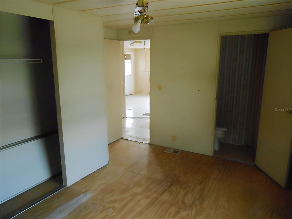 An interior view shows a room with plywood flooring, a closet, and a doorway to a bathroom — 12279 OBRIEN AVENUE, BROOKSVILLE, FL