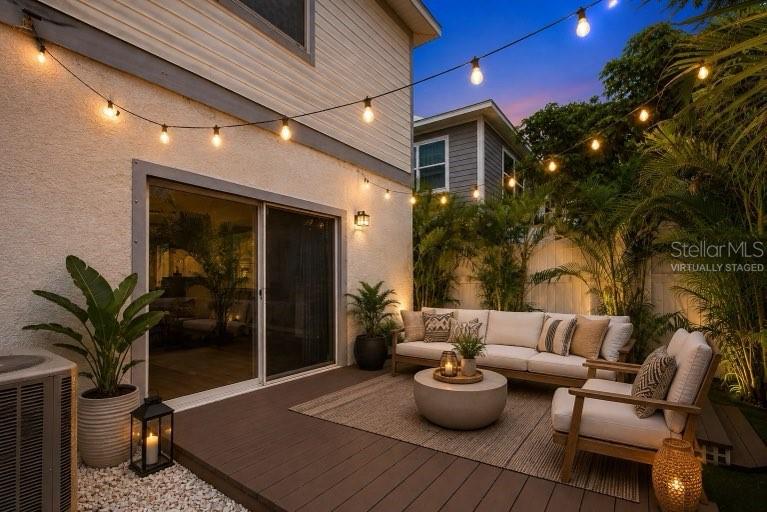 This is a virtually staged outdoor patio featuring a wooden deck, seating area, and string lights — 2704 W GRAY STREET UNIT A, TAMPA, FL