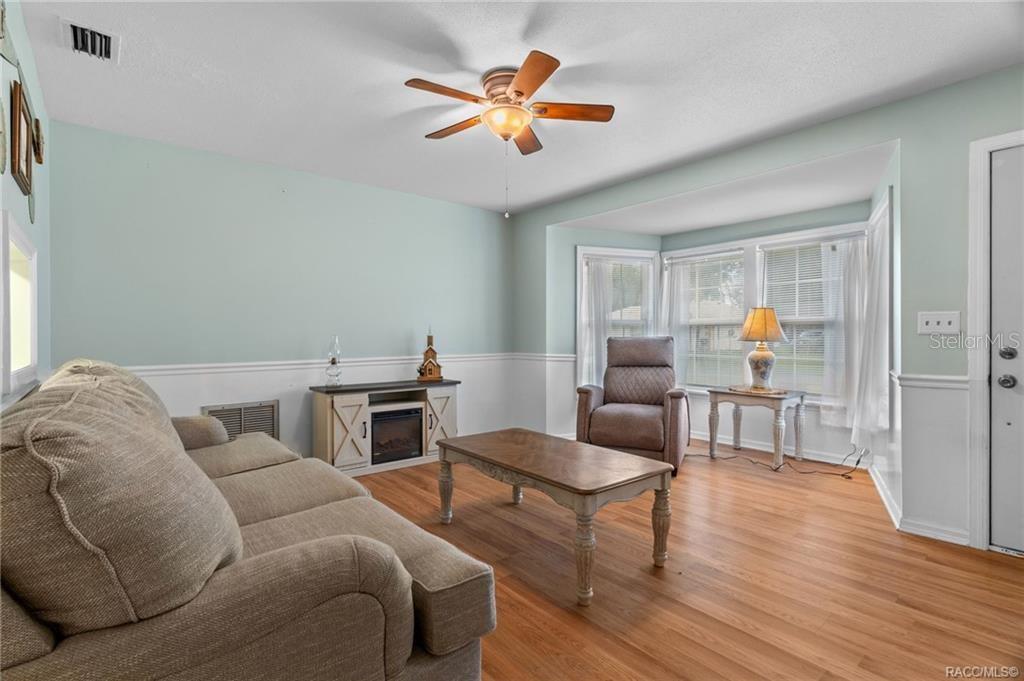 A living room with light blue walls, wood flooring, a ceiling fan, and a fireplace console — 6094 E PENROSE STREET, INVERNESS, FL
