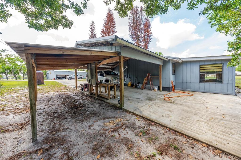 A gray house features a large attached carport with a concrete floor and wooden posts — 3480 ONDICH ROAD, APOPKA, FL