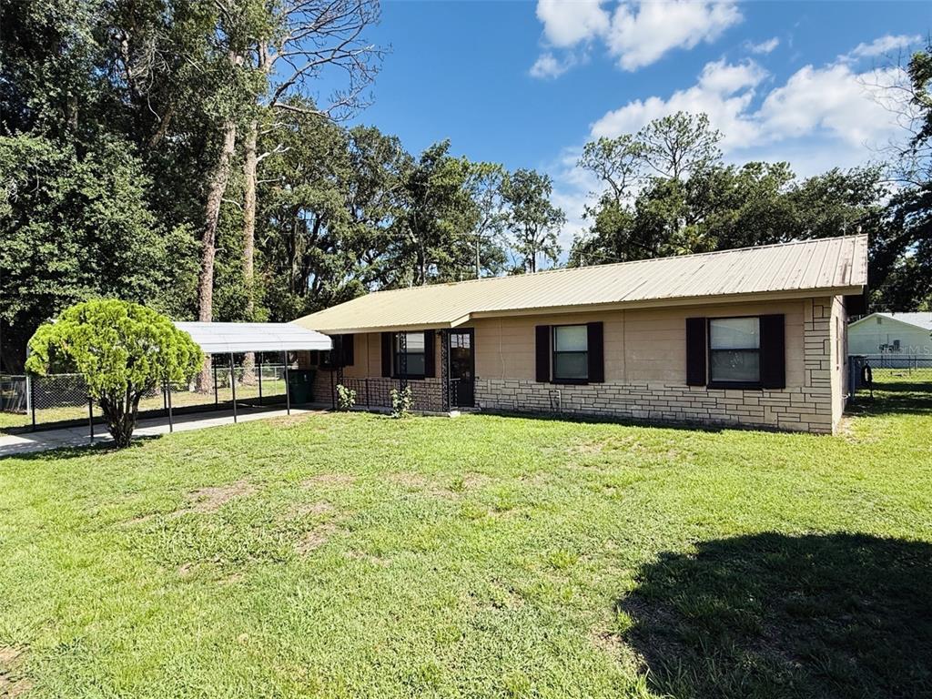 A single-story house with a metal roof, stone facade, and an attached carport — 39048 BLUE JAY AVENUE, ZEPHYRHILLS, FL