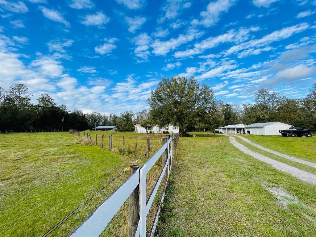 A white fence borders a grassy field leading toward a house and a detached garage — 6814 PEARSON LANE, WESLEY CHAPEL, FL
