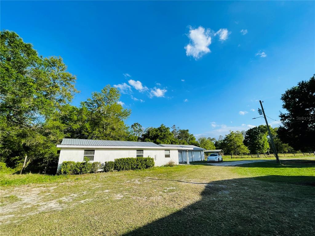 A white single-story house with a metal roof sits on a grassy lot — 6814 PEARSON LANE, WESLEY CHAPEL, FL