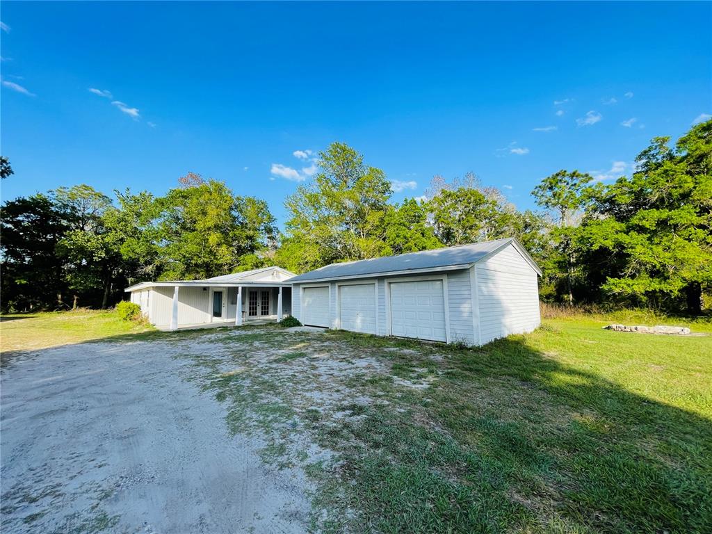 A light-colored house with a three-car garage sits on a grassy lot with trees — 6814 PEARSON LANE, WESLEY CHAPEL, FL