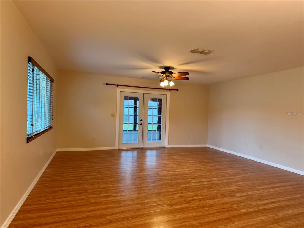 An empty room features wood-look flooring, a ceiling fan, and French doors leading outside — 9940 SW 102ND LANE, OCALA, FL