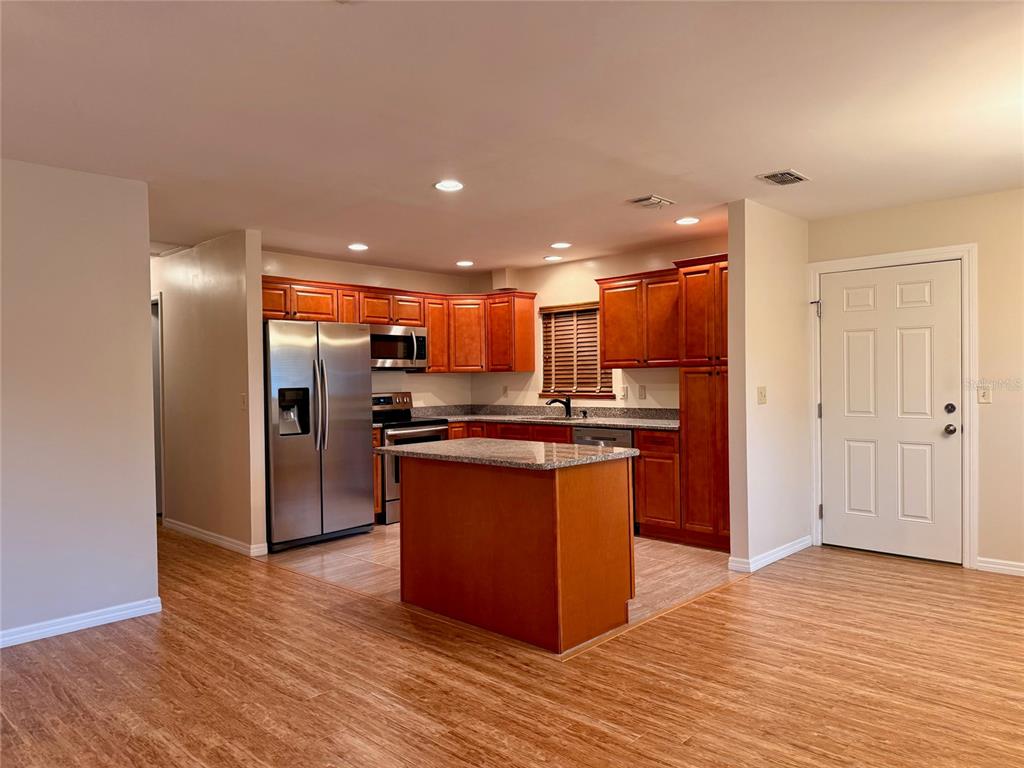 A kitchen with wood cabinets, stainless steel appliances, a center island, and wood-look flooring — 9940 SW 102ND LANE, OCALA, FL