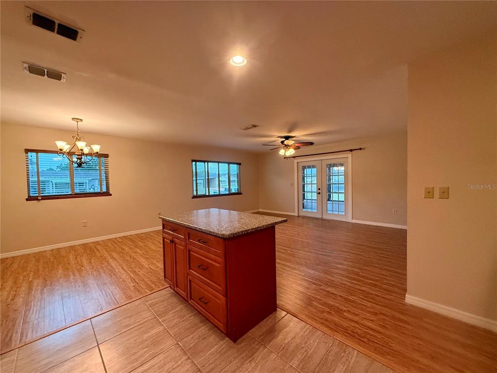 An open-concept room features a kitchen island with granite countertops, wood-look flooring, and French doors — 9940 SW 102ND LANE, OCALA, FL