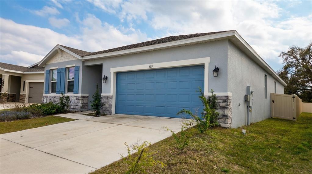 A single-story house with a blue garage door, gray stucco siding, and stone accents — 693 CROWN ROSE DRIVE, EAGLE LAKE, FL