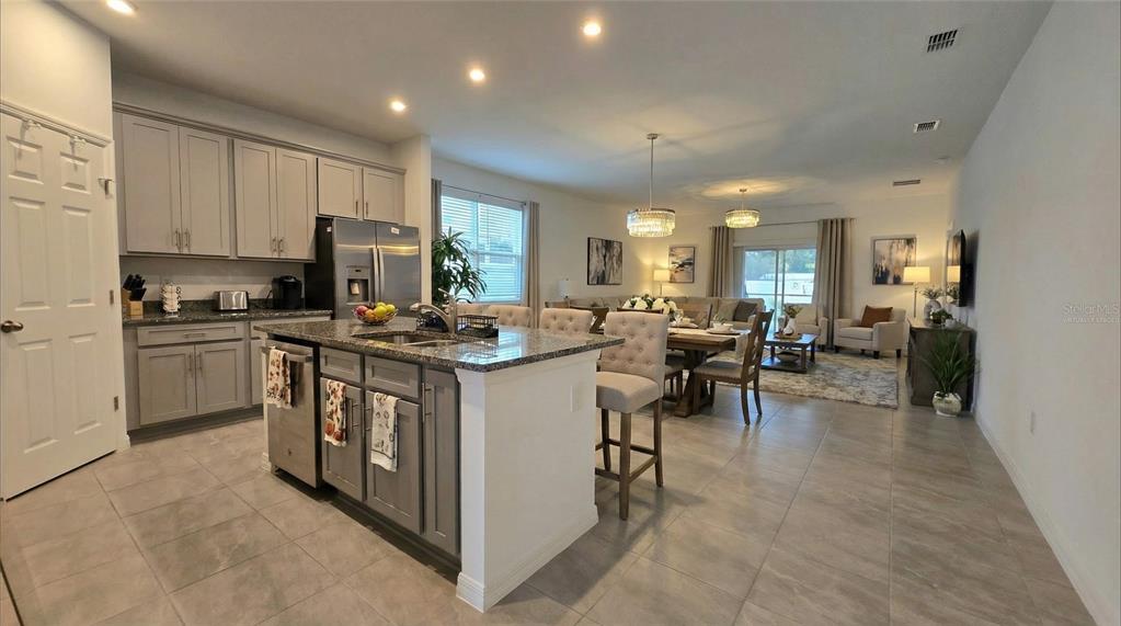 An open-concept kitchen with gray cabinets and granite countertops overlooks a dining and living area — 693 CROWN ROSE DRIVE, EAGLE LAKE, FL