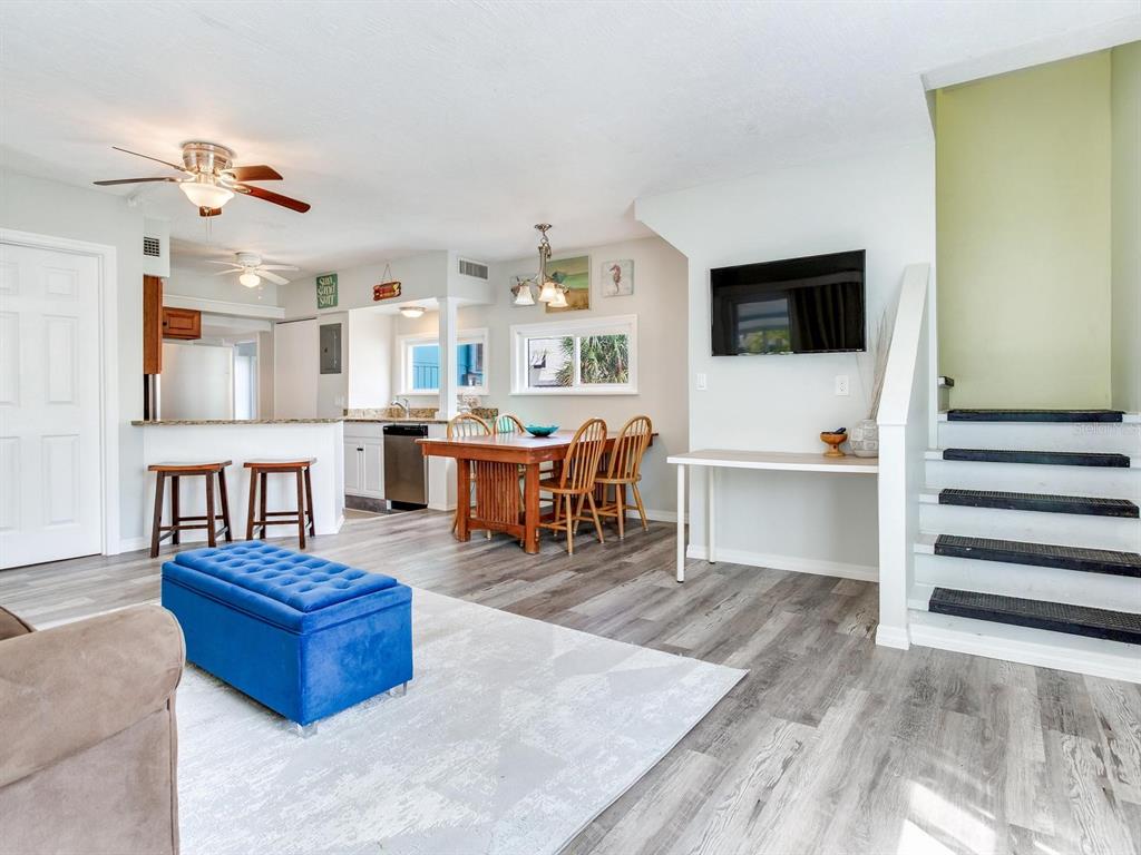 An open-concept living and dining area features wood-look flooring, a blue ottoman, and stairs — 120 93RD AVENUE, TREASURE ISLAND, FL
