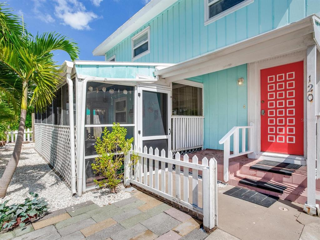 A light blue house features a red front door, a screened porch, and white fencing — 120 93RD AVENUE, TREASURE ISLAND, FL