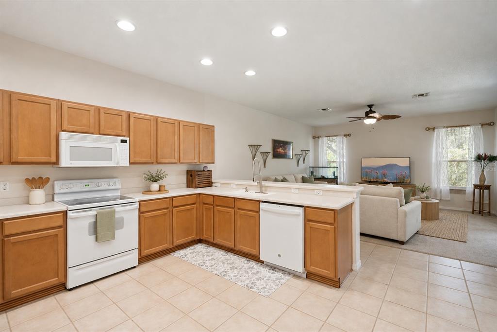 A kitchen with light wood cabinets and white appliances opens into a carpeted living area — 2589 CORBYTON COURT, ORLANDO, FL